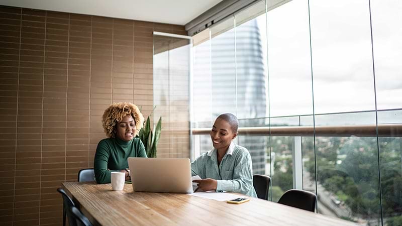 Two women sitting at boardroom table looking at a laptop screen
